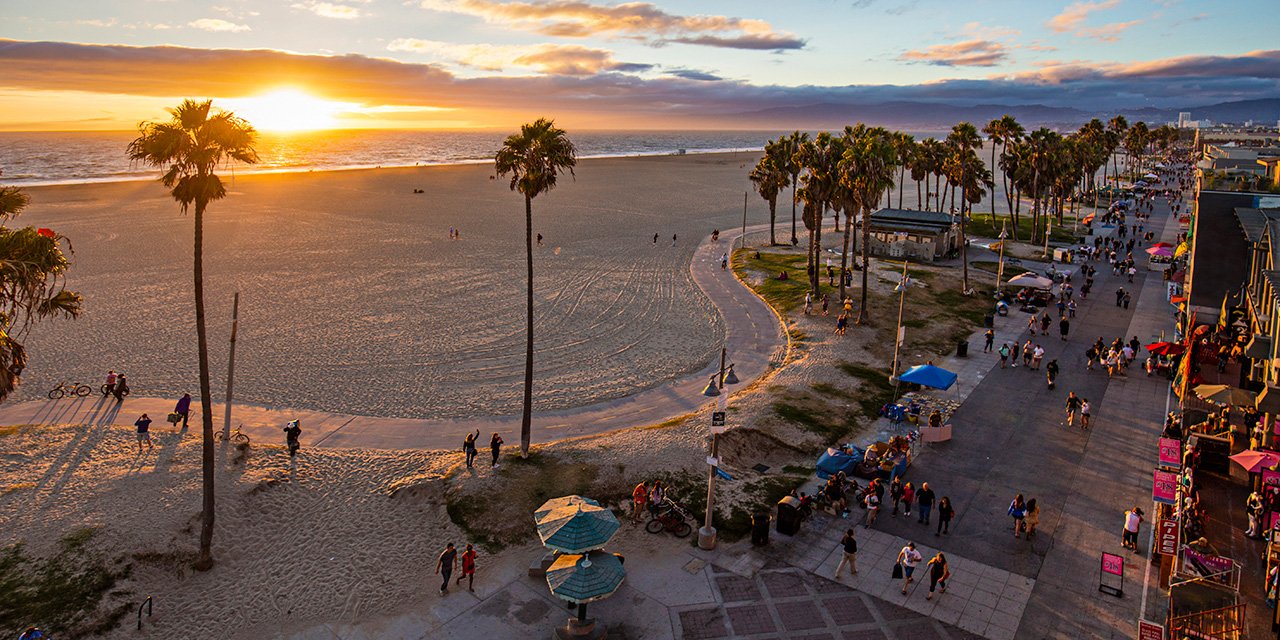 High angle view of Venice beach during sunset. Tourists are walking on footpath by ocean. Shot of beautiful nature and people is taken from above.